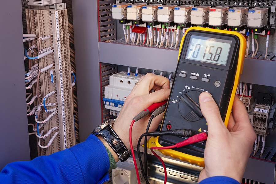 Multimeter in hands of electrician engineer in electrical cabinet. Maintenance of electric system. Worker tests of electrical circuit. Electrician with tester in hands